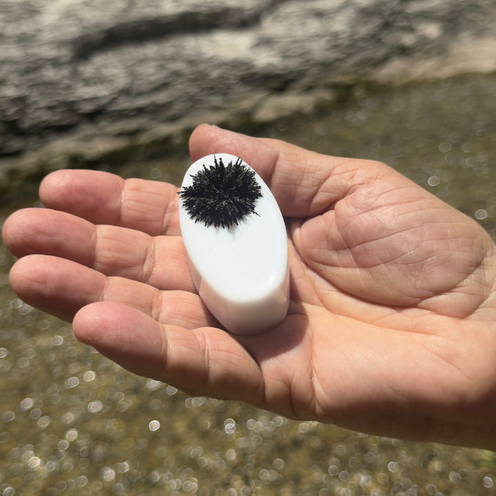Magic Mag black sand magnet held in hand with magnetite clinging to its face