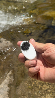 Magic Mag covered in black sand held above a clear creek