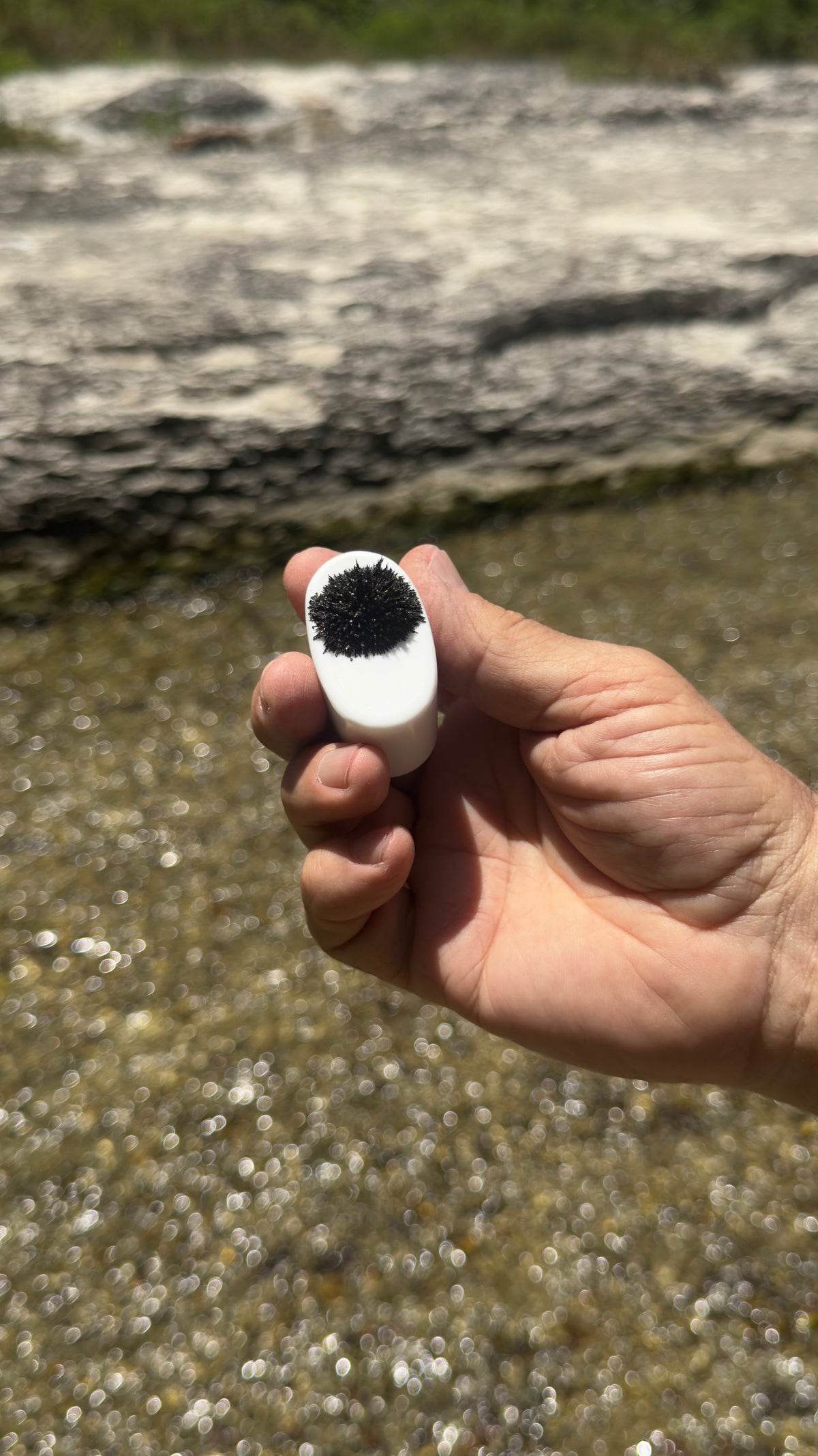 Pocket Mag covered in black sand held above a clear creek